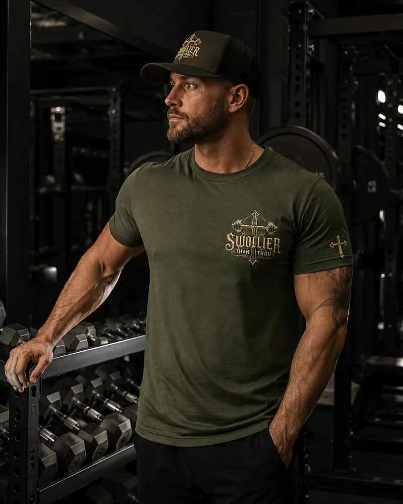 Man in the military green Swollier Than Thou tee and cap beside a dumbbell rack